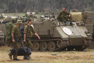 Israeli soldiers carry their gear past an armoured personel carrier as they head home near the border with Gaza