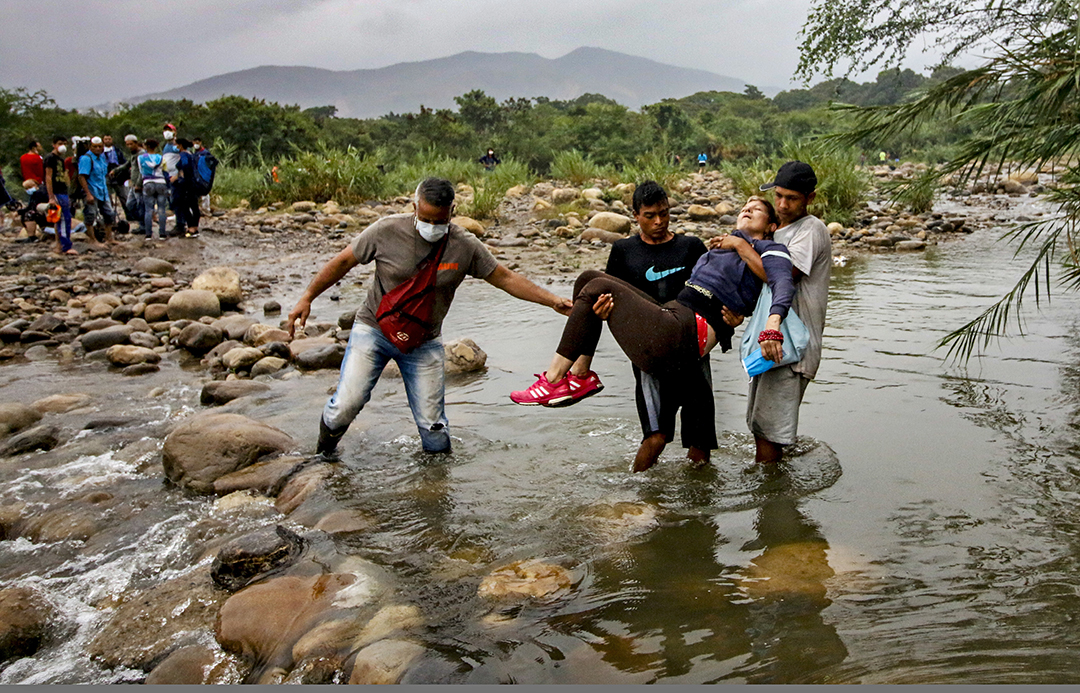 Venezuelan citizens wearing protective face masks to prevent the spread of Coronavirus carry an unconscious lady as they try to enter to Colombia, in Cucuta, Colombia, on March 14, 2020. - Colombian President Ivan Duque announced on Friday, March 13, 2020, the closure of all border crossings with Venezuela, and restricted the entry of foreigners who have been in Europe and Asia in the last 14 days, as measures to stop the expansion of the new Coronavirus. Photo: AFP