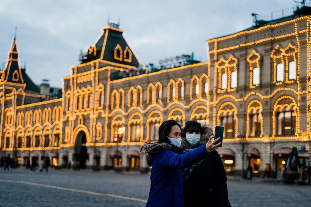 Two women wearing protective face masks to protect from the novel coronavirus, COVID-19, use their smartphone to take a selfie while standing on Red Square in downtown Moscow on March 18, 2020. Dimitar DILKOFF / AFP