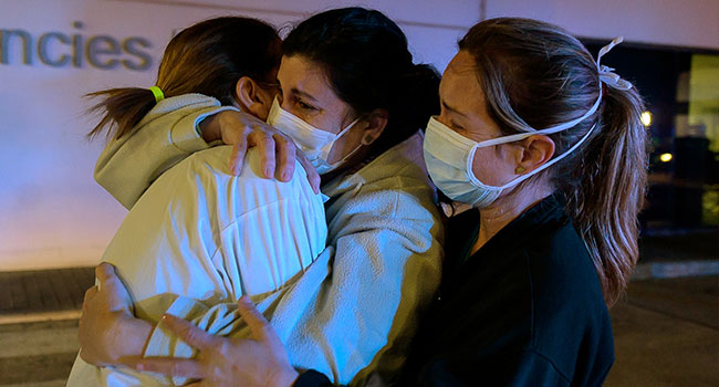 Healthcare workers dealing with the new coronavirus crisis in Spain, hug each other as they are cheered on by people outside La Fe hospital in Valencia on March 26, 2020.