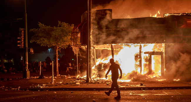 A man walks past a liquor store in flames near the Third Police Precinct on May 28, 2020 in Minneapolis, Minnesota, during a protest over the death of George Floyd. Kerem Yucel / AFP