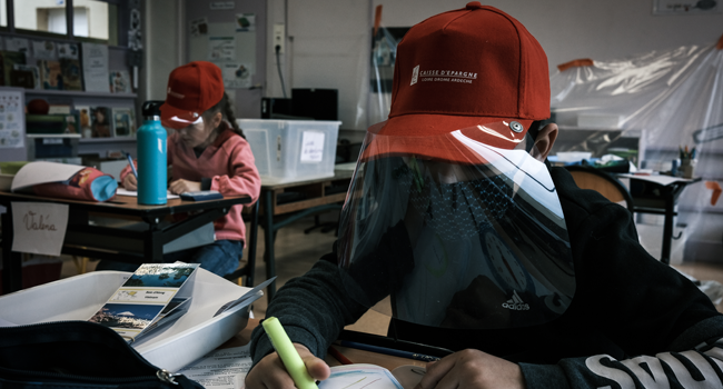 Primary school pupils attend a class wearing protective visor caps made by the city council in La Grand-Croix, near Saint-Etienne, central France, on May 12, 2020. JEAN-PHILIPPE KSIAZEK / AFP
