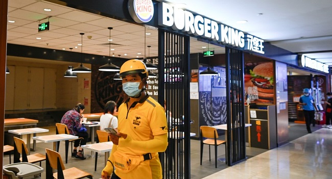 A delivery man wearing a face mask walks past a Burger King restaurant in a mall in Beijing on July 17, 2020. - Burger King has apologised to customers in China after state media reported that two of its restaurants sold expired food in the country, causing an uproad on social media. (Photo by WANG Zhao / AFP)