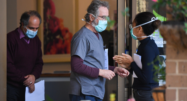 People wearing face masks are seen at the entrance of the Menarock Life aged care facility, where a cluster of some 28 new infections had been reported, in the Melbourne suburb of Essendon on July 14, 2020, as the city battles fresh outbreaks of the COVID-19 coronavirus. William WEST / AFP