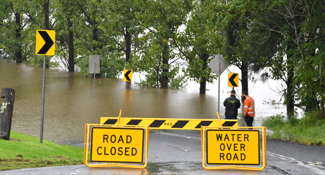 Workers look at an inundated main road by floodwaters in Richmond suburb on March 22, 2021, as Sydney braced for its worst flooding in decades after record rainfall caused its largest dam to overflow and as deluges prompted mandatory mass evacuation orders along Australia's east coast. Saeed KHAN / AFP