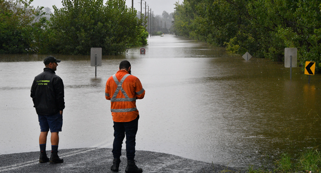 Workers look at an inundated main road by floodwaters in Richmond suburb on March 22, 2021, as Sydney braced for its worst flooding in decades after record rainfall caused its largest dam to overflow and as deluges prompted mandatory mass evacuation orders along Australia's east coast. Saeed KHAN / AFP