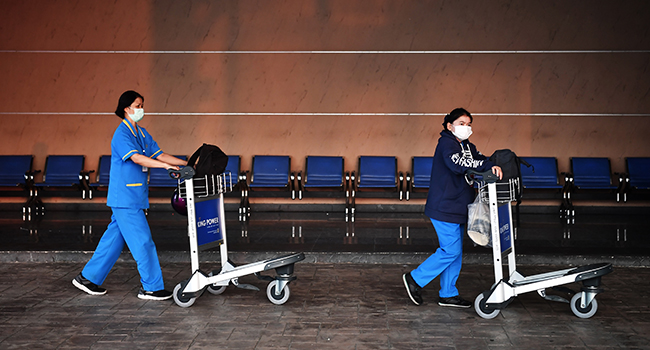 People wearing protective facemasks walk outside U-Tapao Airport in Rayong on February 4, 2020, where Thais nationals who had been evacuated from Wuhan, the epicentre of the novel coronavirus outbreak, are expected to arrive. Lillian SUWANRUMPHA / AFP