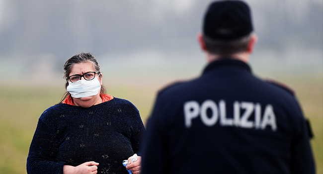 A resident wearing a respiratory mask (L) talks with a police officer giving informations at the entrance of the small town of Casalpusterlengo, southeast of Milan, on February 23, 2020. Miguel MEDINA / AFP