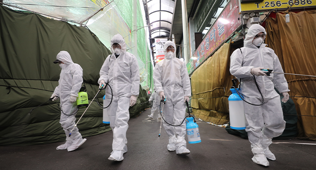 Market workers wearing protective gear spray disinfectant at a market in the southeastern city of Daegu on February 23, 2020 as a preventive measure after the COVID-19 coronavirus outbreak. YONHAP / AFP