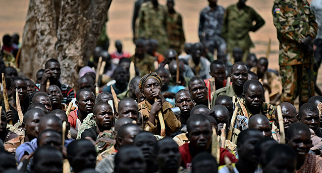 Trainee soldiers for a new unified army sit on the ground with their wooden rifles while attending a reconciliation programme run by the United Nations Mission in South Sudan (UNMISS) at a makeshift barracks in Mapel on January 31, 2020. TONY KARUMBA / AFP