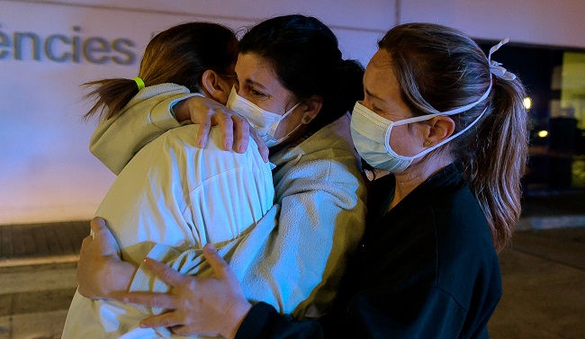 Healthcare workers dealing with the new coronavirus crisis in Spain, hug each other as they are cheered on by people outside La Fe hospital in Valencia on March 26, 2020. - Spain's coronavirus toll surged above 4,000 today but the increase in both fatalities and infections slowed, raising hope a nationwide lockdown was starting to curb the spread of the epidemic. Spain currently has the world's second highest death toll after Italy, and has so far suffered 4,089 deaths after another 655 people succumbed to the virus in the past 24 hours, the health ministry said. (Photo by JOSE JORDAN / AFP)