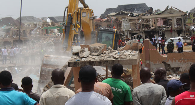 Bystanders watched as an excavator tried to pick through the rubble on Monday 16, 2020. Photo Credit: Solomon Elusoji / Channels TV