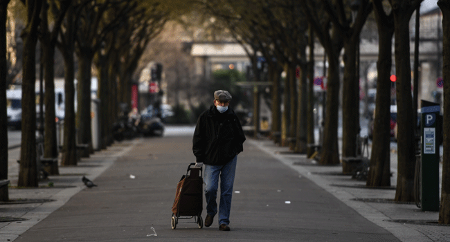 An elderly man wearing a face mask pulls a trolley on his way to a market in Paris on March 19, 2020, as a strict lockdown is in effect in France to stop the spread of COVID-19, caused by the novel coronavirus. Christophe ARCHAMBAULT / AFP