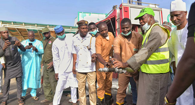 Abdullahi Ganduje (right) holds a hose on Saturday, March 28, 2020.