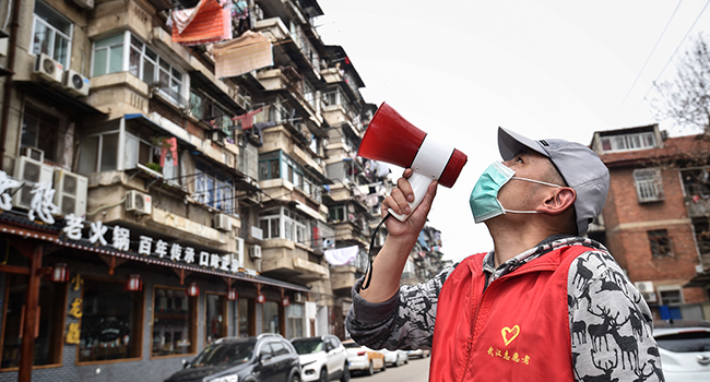 A community volunteer informs residents to get vegetables with a loudspeaker in Wuhan, in China's central Hubei province on March 13, 2020. STR / AFP