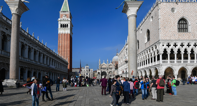 In this file photo taken on November 04, 2019 tourists walk across St Mark's Square (Piazza San Marco) by St. Mark's Campanile (Rear L), St. Mark's Basilica (Basilica San Marco, Rear R) and the Doge's Palace (Palazzo Ducale, R) in Venice. MIGUEL MEDINA / AFP