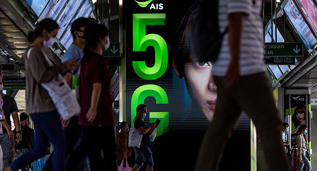 Commuters walk in front of a 5G advertisement screen at a train station in Bangkok on May 5, 2020. Mladen ANTONOV / AFP