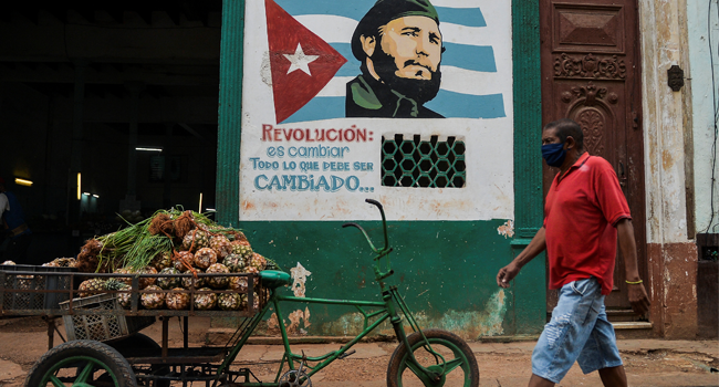 A man wearing a face mask walks near a sign depicting Cuban late leader Fidel Castro and reading “Revolution is to change everything that needs to be changed”, in Havana on May 13, 2020, amid the new coronavirus pandemic.  YAMIL LAGE / AFP