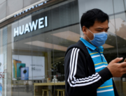 A man wearing a face mask uses his mobile phone as he walks past a Huawei store in Beijing on May 16, 2020. WANG Zhao / AFP