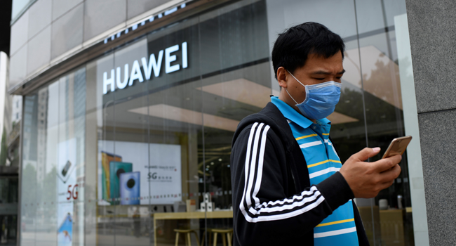 A man wearing a face mask uses his mobile phone as he walks past a Huawei store in Beijing on May 16, 2020. WANG Zhao / AFP