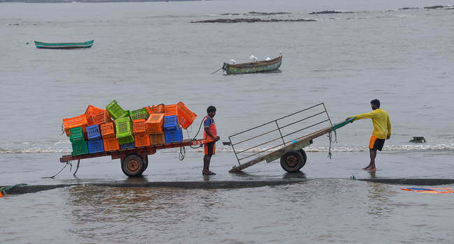 Fishermen chat while they meet halfway on a pier as they offload crates towards inland ahead of a cyclonic storm that may hit the North Maharashtra and Gujarat coast, at the Madh fishing village, in the north western coast of Mumbai on June 2, 2020. INDRANIL MUKHERJEE / AFP