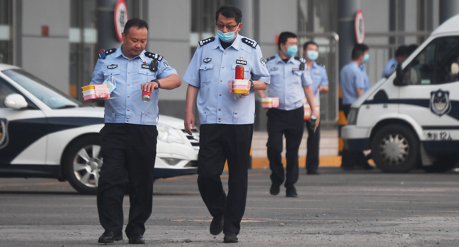 Police officers carry food as they walk in the grounds of a closed bus station near the closed Xinfadi market in Beijing on June 13, 2020.  GREG BAKER / AFP