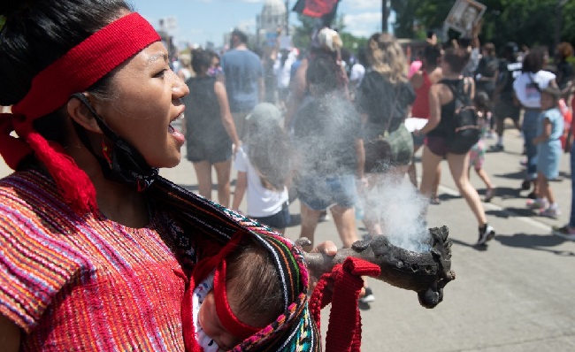 Maryanne Quiroz, a member of the traditional Azteca dance group Yaocenoxtli, holding her 2-month old daughter Tekpani, uses incense to cleanse energy during a National Mothers March in St. Paul, Minnesota July 12, 2020. - Mothers, and families, who have lost loved ones to police violence are answering the call made by George Floyd for his mother, seen around the world in the video of his arrest where, Floyd, a 46-year-old black man suspected of passing a counterfeit $20 bill, died in Minneapolis on May 25, 2020. (Photo by Amanda Sabga / AFP)