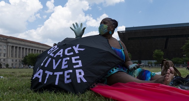 A woman sits near her umbrella during a small rally against racism in the US next to the Washington Memorial in Washington, DC, on July 4, 2020, ahead of the Independence Day celebrations. - Wide spread national protests over police brutality and systemic racism have taken place following the police killing of George Floyd in Minneapolis in May. (Photo by ROBERTO SCHMIDT / AFP)