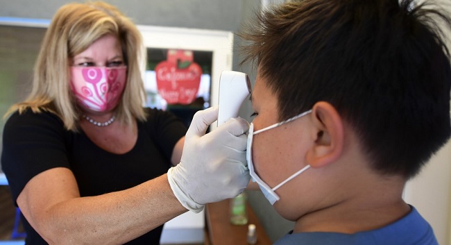 Principal Pam Rasmussen (L) takes the temperature of arriving students as per coronavirus guidelines during summer school sessions at Happy Day School in Monterey Park, California on July 9, 2020. - California Governor Gavin Newsom says the reopening of California schools for the coming school year will be based on safety and not pressure from President Donald Trump as California sets records for one-day increases in COVID-19 cases. (Photo by Frederic J. BROWN / AFP)