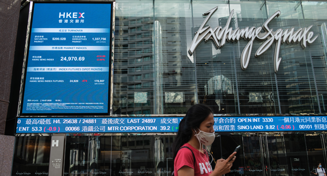 A woman wearing a face mask walks past a stocks display board outside Exchange Square in Hong Kong on July 16, 2020, as the city experiences another spike in COVID-19 coronavirus cases. Anthony WALLACE / AFP