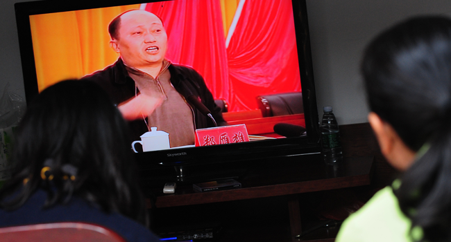 This file photo taken on December 20, 2011 shows Zheng Yanxiong, then-Communist Party Secretary of Shanwei prefecture, speaking on television as villagers watch the broadcast in Wukan, Guangdong province. MARK RALSTON / AFP