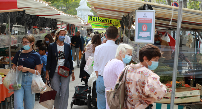 People wearing face masks walk past a sign displaying sanitary rules on a market in Paris, on August 27, 2020, as face masks will become mandatory in the city. Ludovic MARIN / AFP