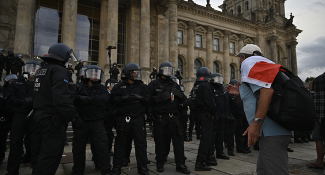 A man wrapped in a black-white-red flag leans towards the German riot policemen standing guard in front of the Reichstag building, which houses the Bundestag lower house of parliament, as protesters tried to storm in at the end of a demonstration called by far-right and COVID-19 deniers to protest against restrictions related to the new coronavirus pandemic, in Berlin, on August 29, 2020.  John MACDOUGALL / AFP