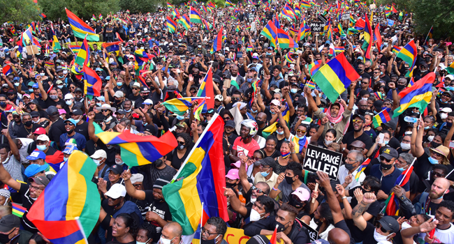 People wave the national flag as they attend a protest against the government's response to the oil spill disaster that happened in early August at St Louis Cathedral in Port Louis, on the island of Mauritius, on August 29, 2020. Beekash Roopun / L'Express Maurice / AFP