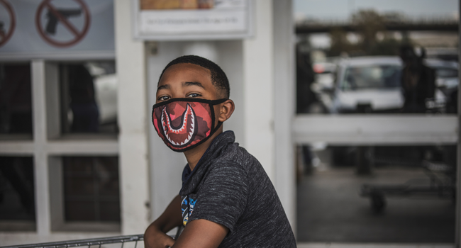 A boy wears a face mask as a preventive measure against the spred of the COVID-19 coronavirus as he queues outside Makro in Soweto, Johannesburg, on March 24, 2020. MARCO LONGARI / AFP