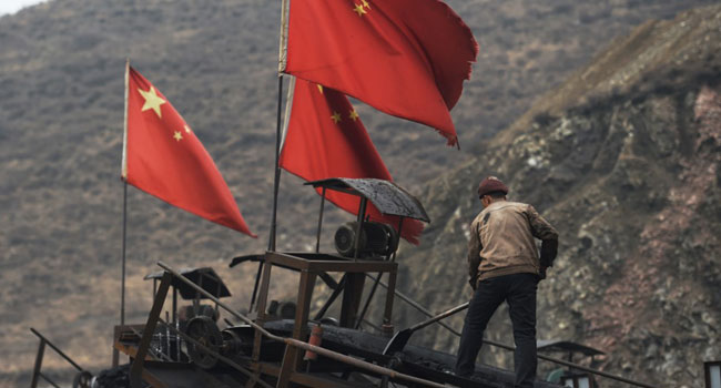 (FILES) This file photo taken on November 20, 2015 shows Chinese flags next to a worker clearing a conveyer belt used to transport coal, near a coal mine at Datong, in China's northern Shanxi province.