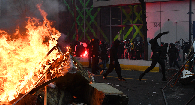 A protester throw a stone near a burning barricade during a demonstration for 'social rights' and against the 'global security' draft law, which Article 24 would criminalise the publication of images of on-duty police officers with the intent of harming their 'physical or psychological integrity', in Paris, on December 5, 2020. Anne-Christine POUJOULAT / AFP