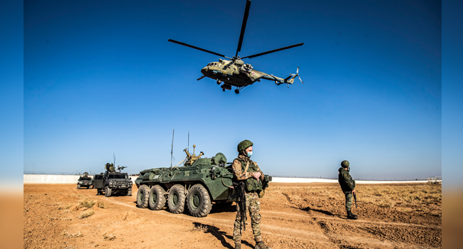 A Russian Mil Mi-17 military helicopter flies by soldiers and military vehicles during a joint Russian-Turkish patrol in the eastern countryside of the town of Darbasiyah near the border with Turkey in Syria's northeastern Hasakah province on December 7, 2020. Delil SOULEIMAN / AFP