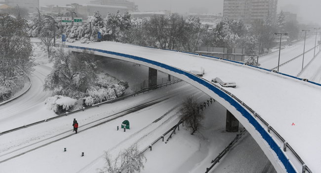 Two people walk along the M30 ringroad amid a heavy snowfall in Madrid on January 9, 2021. PIERRE-PHILIPPE MARCOU / AFP