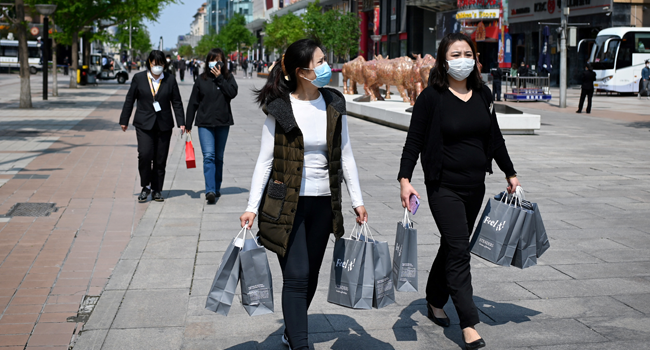 This file photo taken on April 17, 2020 shows two pedestrians carrying shopping bags along a street in Beijing. WANG ZHAO / AFP