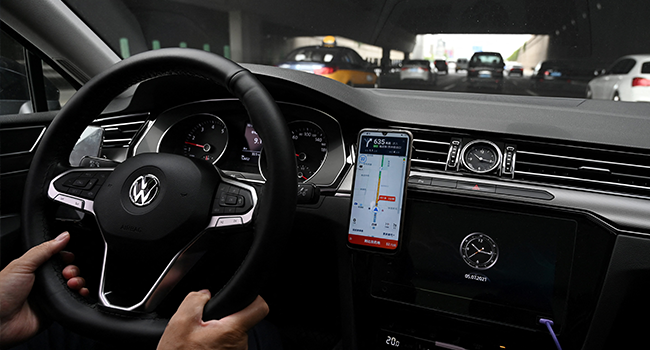 A driver uses the map on the Didi Chuxing ride-hailing app on his smartphone while driving on a street in Beijing on July 5, 2021. GREG BAKER / AFP