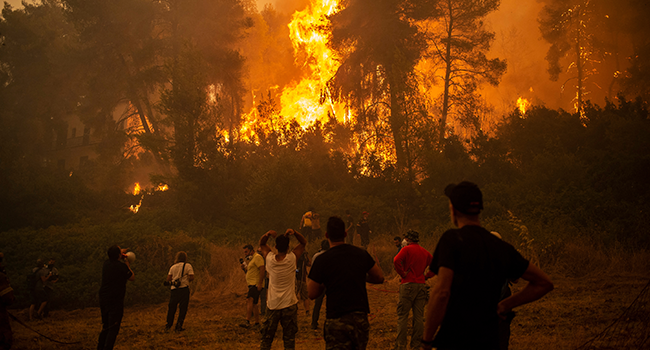 A local uses a megaphone as others observe a large forest fire approaching the village of Pefki on Evia (Euboea) island, Greece's second largest island, on August 8, 2021. ANGELOS TZORTZINIS / AFP