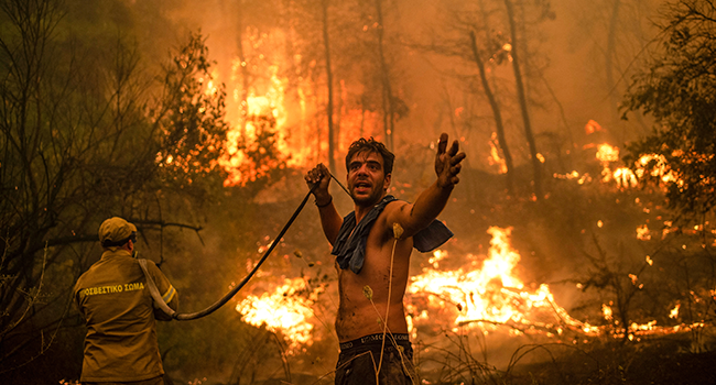 A local resident gestures as he holds n empty water hose during an attempt to extinguish forest fires approaching the village of Pefki on Evia (Euboea) island, Greece's second largest island, on August 8, 2021. ANGELOS TZORTZINIS / AFP