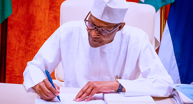 A photo released by the State House on August 16, 2021 showing President Muhammadu Buhari signing the Petroleum Industry Bill into law. Bayo Omoboriowo/State House