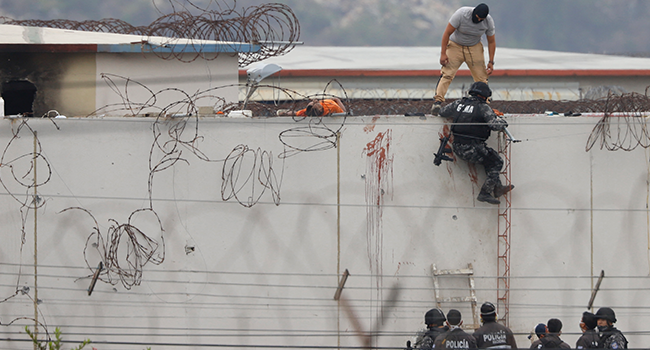 Members of the Ecuadorian police are seen next to the body of an inmate on the roof of a pavilion of the Guayas 1 prison in Guayaquil, Ecuador, on November 13, 2021. Nicola Gabirrete / AFP