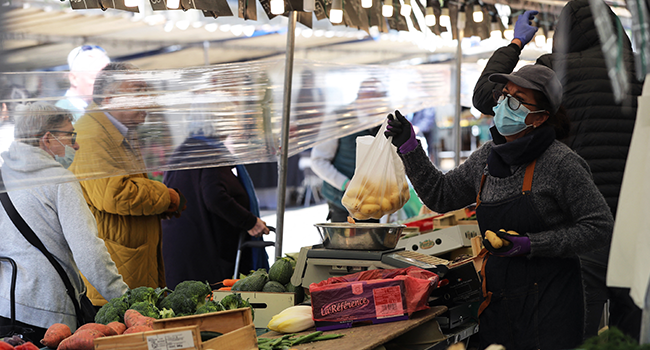 In this file photo taken on May 14, 2020, a produce vendor holds a plastic bag containing potatoes as she serves clients behind a plastic sheet at a street market on the Saxe Avenue in Paris. Ludovic MARIN / AFP