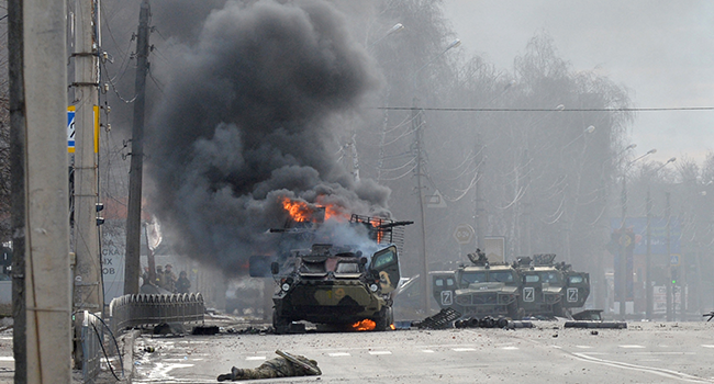 This photograph taken on February 27, 2022 shows a Russian Armoured personnel carrier (APC) burning next to unidentified soldier's body during fight with the Ukrainian armed forces in Kharkiv. Sergey BOBOK / AFP
