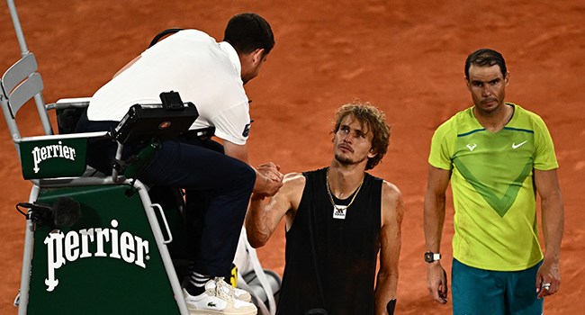Germany's Alexander Zverev (C) shakes hands with umpire Renaud Lichtenstein (L) as he walks on crutches after being injured during his men's semi-final singles match against Spain's Rafael Nadal (R) on day thirteen of the Roland-Garros Open tennis tournament at the Court Philippe-Chatrier in Paris on June 3, 2022. Anne-Christine POUJOULAT / AFP