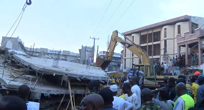 A crowd watches on as an excavator picks through the rubble after a building collapsed in Kano on August 30, 2022.