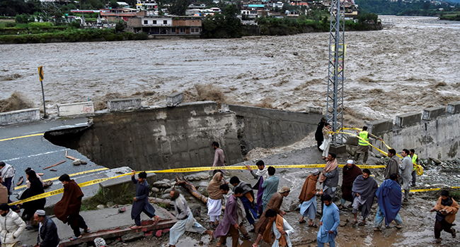 People gather in front of a road damaged by flood waters following heavy monsoon rains in Madian area in Pakistan's northern Swat Valley on August 27, 2022. Photo by Abdul MAJEED / AFP